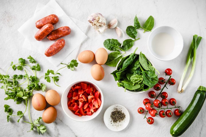 ingredients such as eggs, chorizo, herbs and vegetables on a table