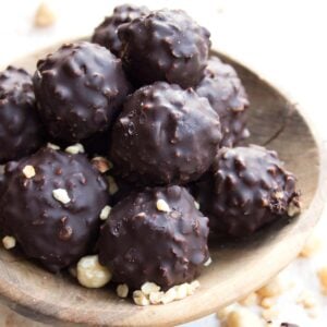 a bowl filled with keto Ferrero Rocher truffles with a chopped hazelnut and dark chocolate coating