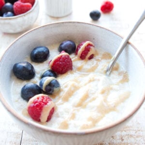 keto oatmeal made with coconut flour in a bowl topped with blueberries and raspberries and a spoon