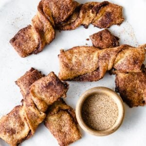 keto snickerdoodle twists ona plate with a bowl of cinnamon and sweetener