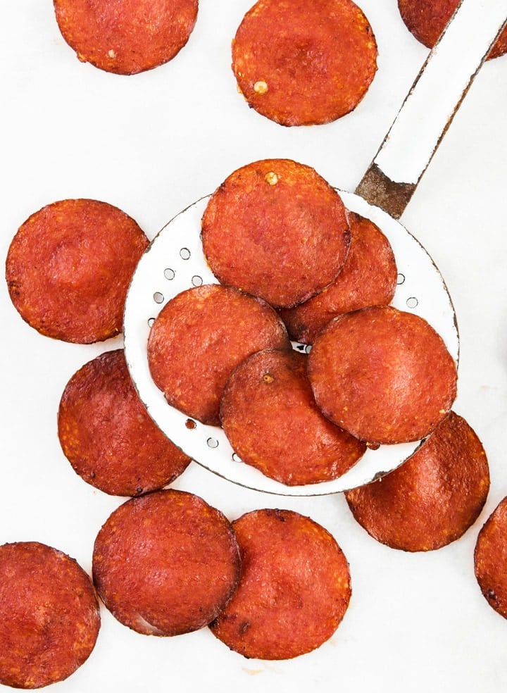 oven-baked pepperoni slices and a slotted spoon