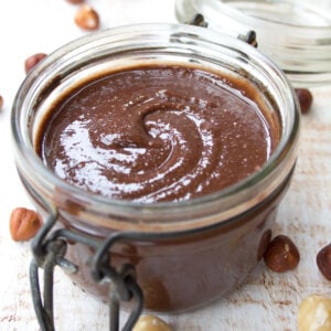 an open glass jar of sugar free nutella with hazelnuts spread over a table