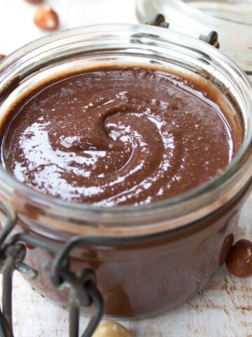an open glass jar of sugar free nutella with hazelnuts spread over a table