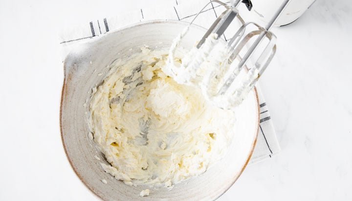 blending cream cheese and butter with an electric mixer in a bowl