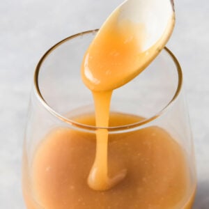 a glass jar with keto caramel sauce and caramel dripping from a spoon
