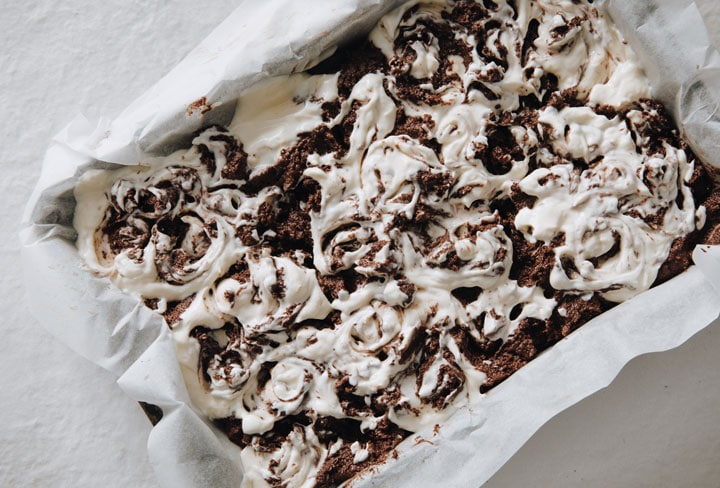 brownie and cheesecake batter swirled together in a pan lined with parchment paper