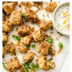 breaded cauliflower florets on parchment paper with a mayonnaise bowl