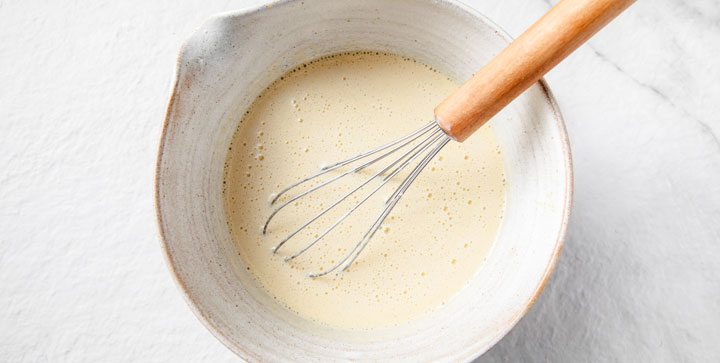whisked frothy egg yolks, vanilla seeds and sweetener in a bowl with a whisk