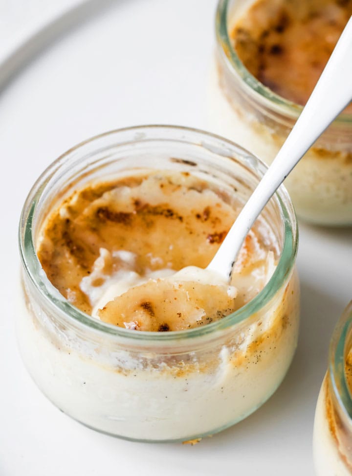 keto creme brulee in a glass jar with a crispy sugar top and a spoon taking a bite