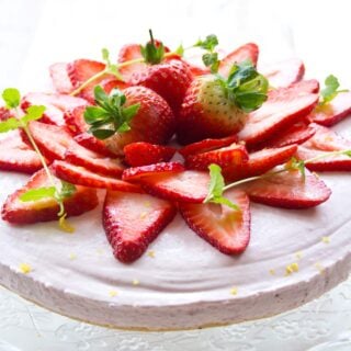 A sugar free strawberry cheesecake topped with sliced strawberries and decorated with mint leaves and lemon zest