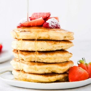 a stack of keto coconut flour pancakes drizzled with sugar free syrup and topped with strawberries