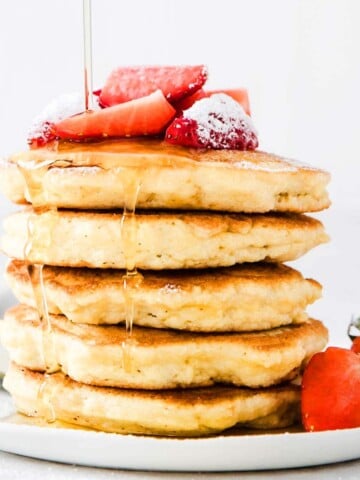 a stack of keto coconut flour pancakes drizzled with sugar free syrup and topped with strawberries
