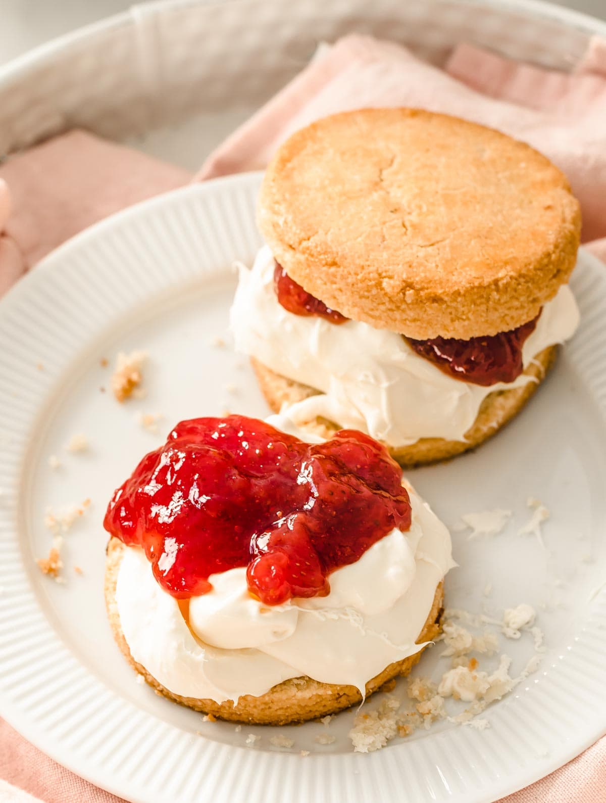 two scones on a plate, filled with clotted cream and strawberry jam