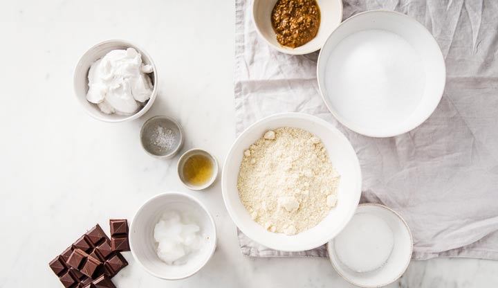 Ingredients such as almond flour, chocolate, sweetener and coconut oil in bowls.