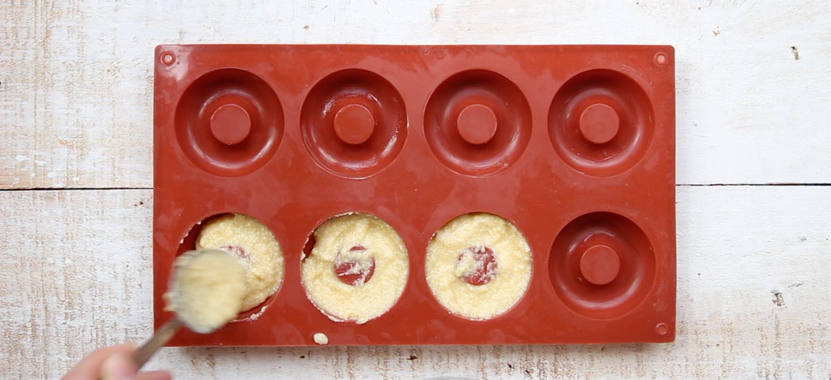 filling donut batter into a donut pan with a spoon