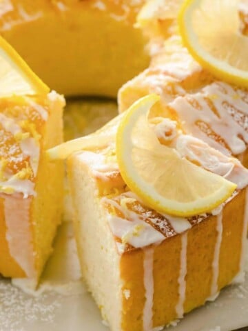 A round Keto lemon pound cake topped with a glaze and lemon slices and a cake piece cut out