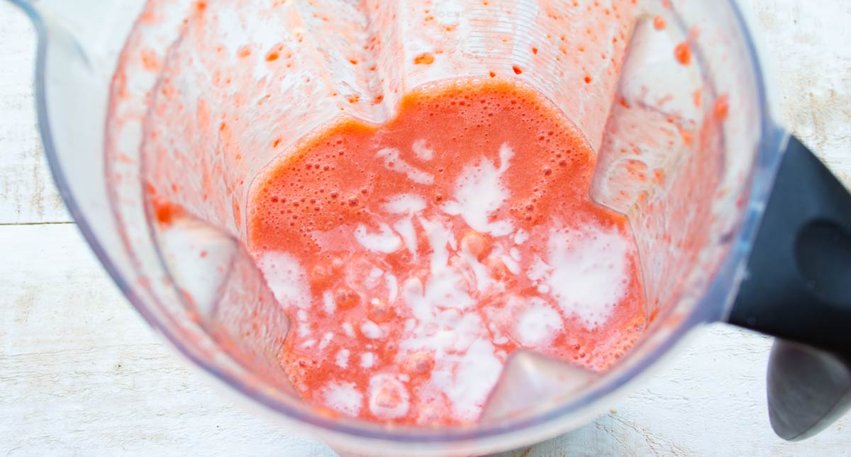 adding coconut cream to the blended strawberry gelatin mix in a food processor jug