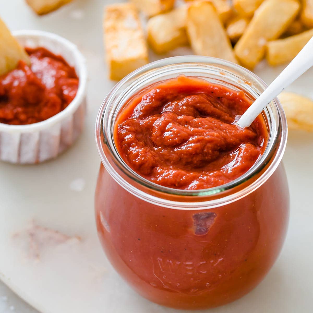 a glass jar of sugar free ketchup and a spoon and turnip fries in the background