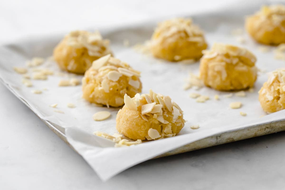 Unbaked cookies topped with almond flakes on a baking sheet lined with parchment paper.