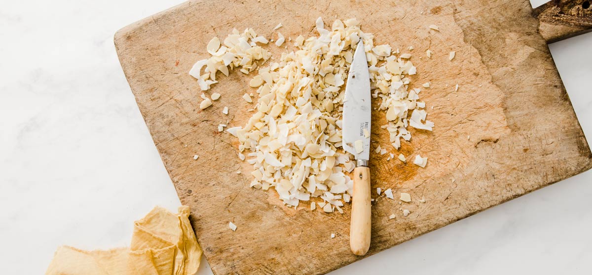 Chopped almond flakes and coconut chips on a wooden board and a knife.