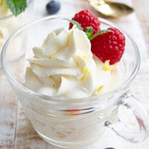 keto cheesecake fluff piped into glass desert cups topped with raspberries, lemon zest and mint leaves