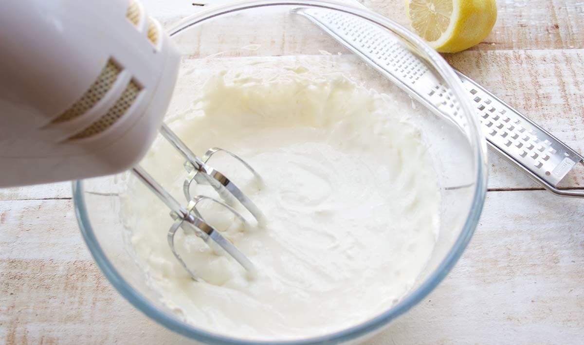 mixing cream cheese, powdered sweetener, lemon and vanilla in a bowl with a mixer