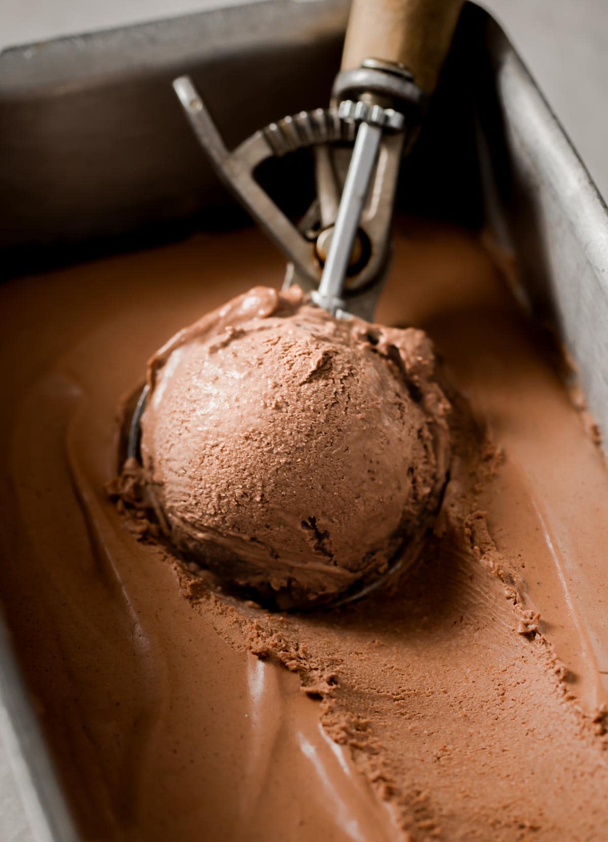 Chocolate low carb ice cream in a rectangular tin and a scoop of ice cream being scooped out
