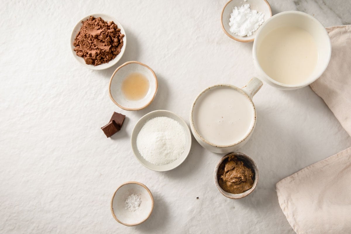almond milk, cacao powder, nut butter, chocolate, collagen powder and sweetener in bowls