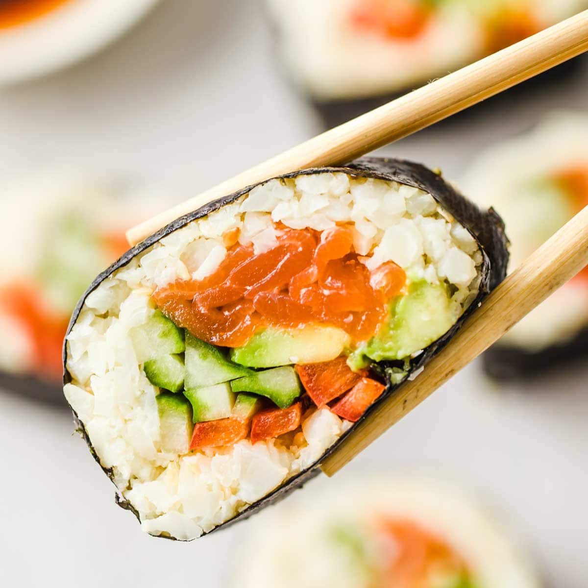 a pair of chopsticks lifting a salmon sushi roll