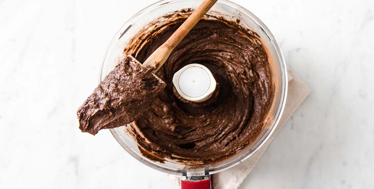 brownie batter in a food processor bowl and a spatula resting on top