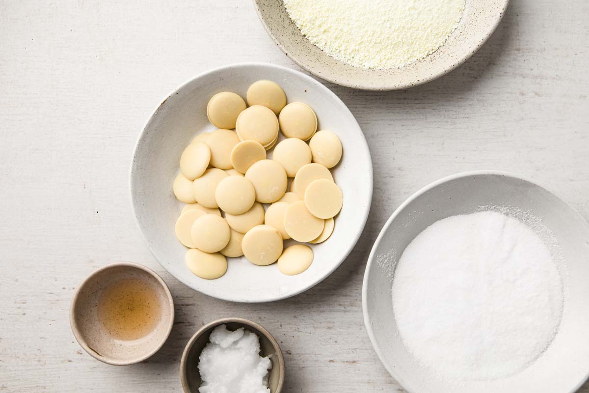 cacao butter drops, sweetener, milk powder and vanilla extract measured in bowls