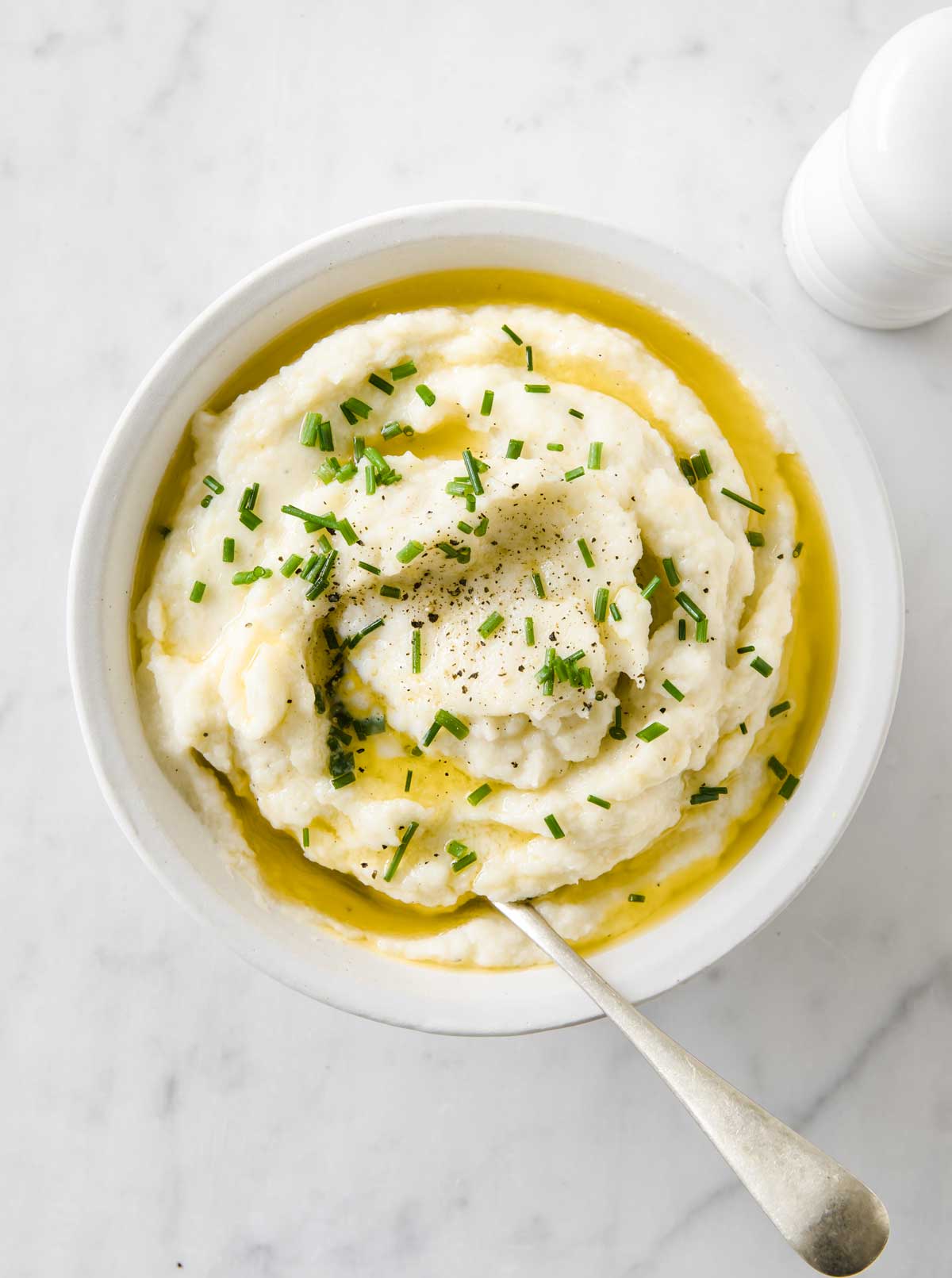 A bowl with cauliflower mash topped with melted butter, chives and a spoon.