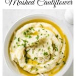 mashed cauliflower in a bowl with melted butter and a spoo