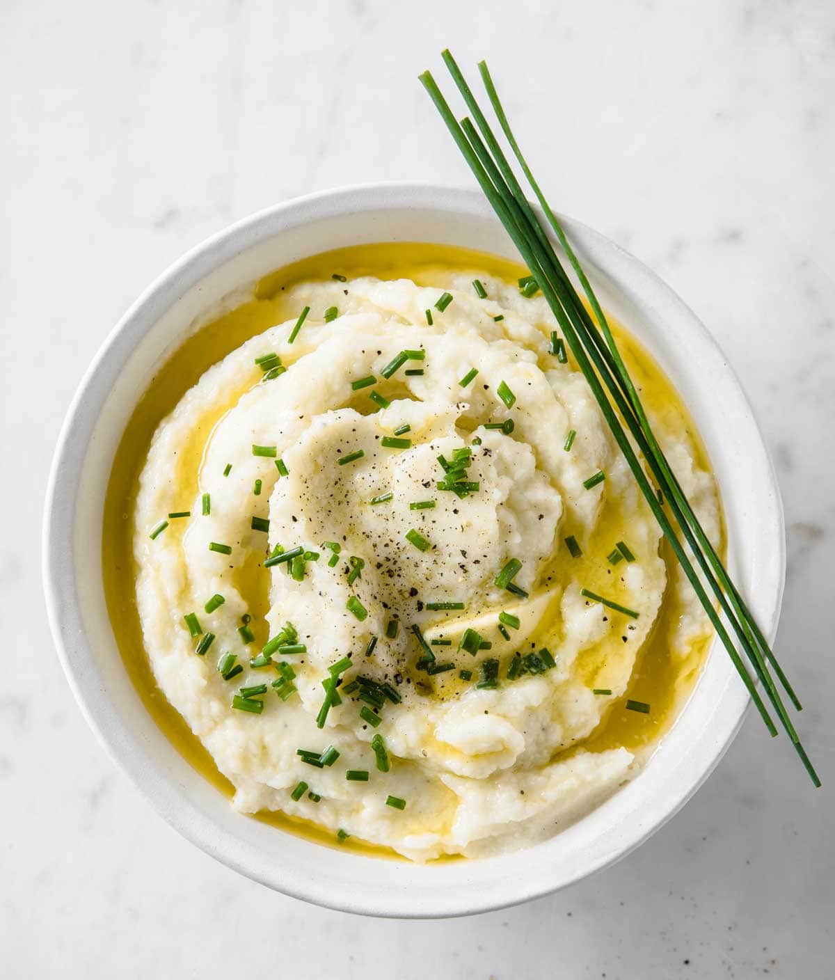 A bowl with mashed cauliflower topped with melted butter and chives.