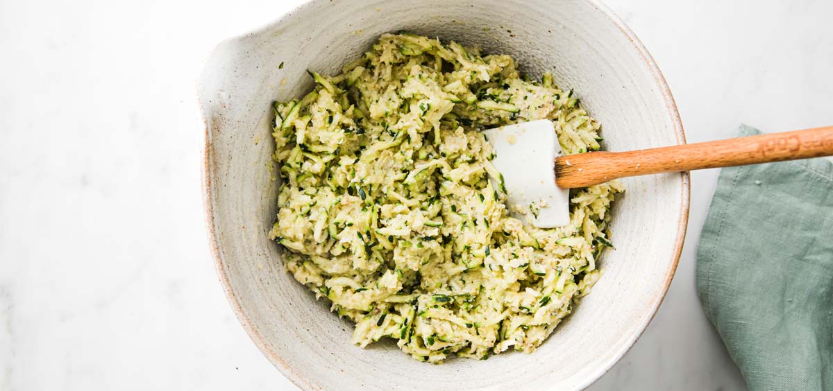 grated zucchini mixed with wgg and almond flour in a bowl and a spatula
