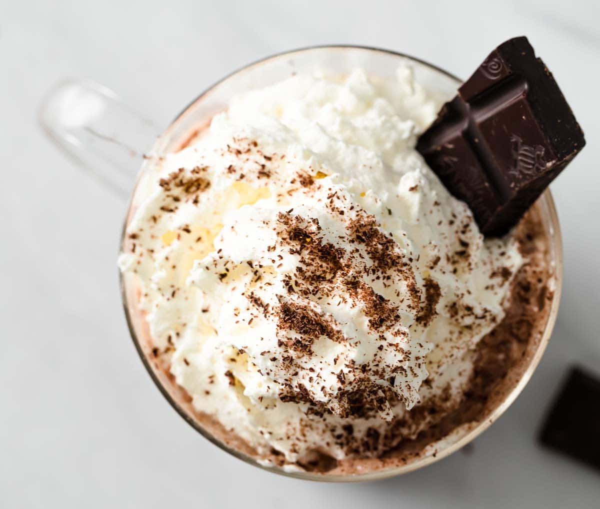 A square of dark chocolate in whipped cream decorating a hot chocolate.