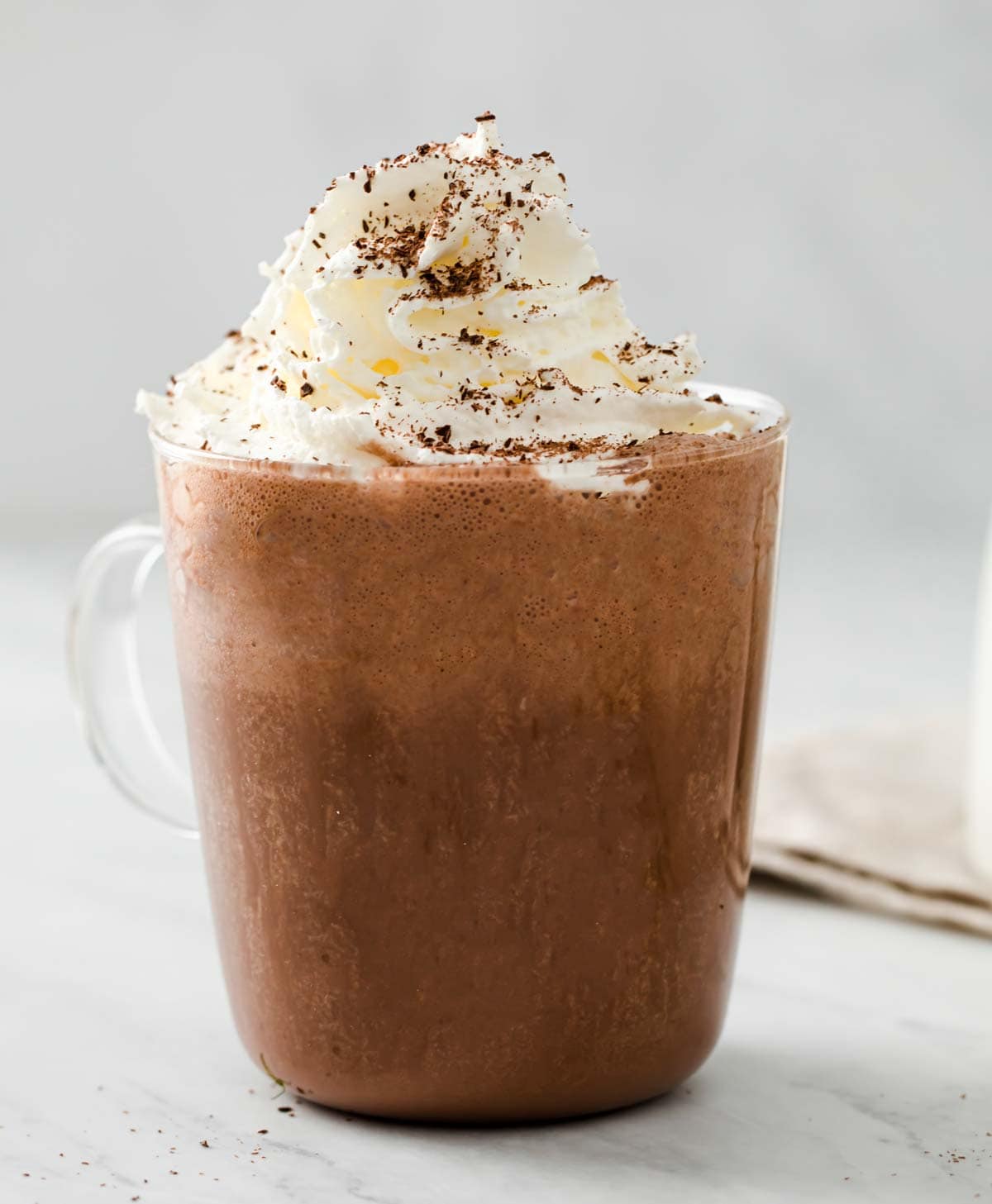 A glass cup filled with frothy hot chocolate topped with cream