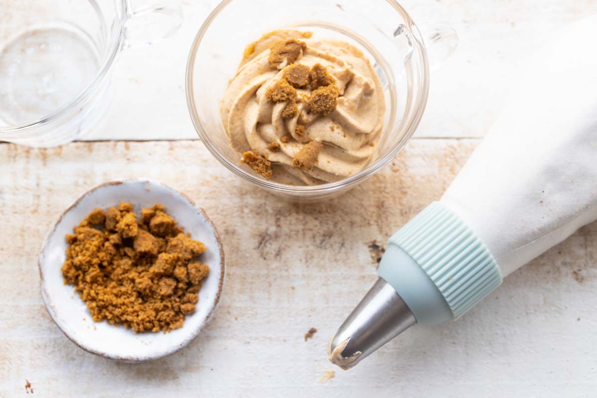 A piping bag, a glass cup with pumpkin mousse and crumbled ginger cookies.