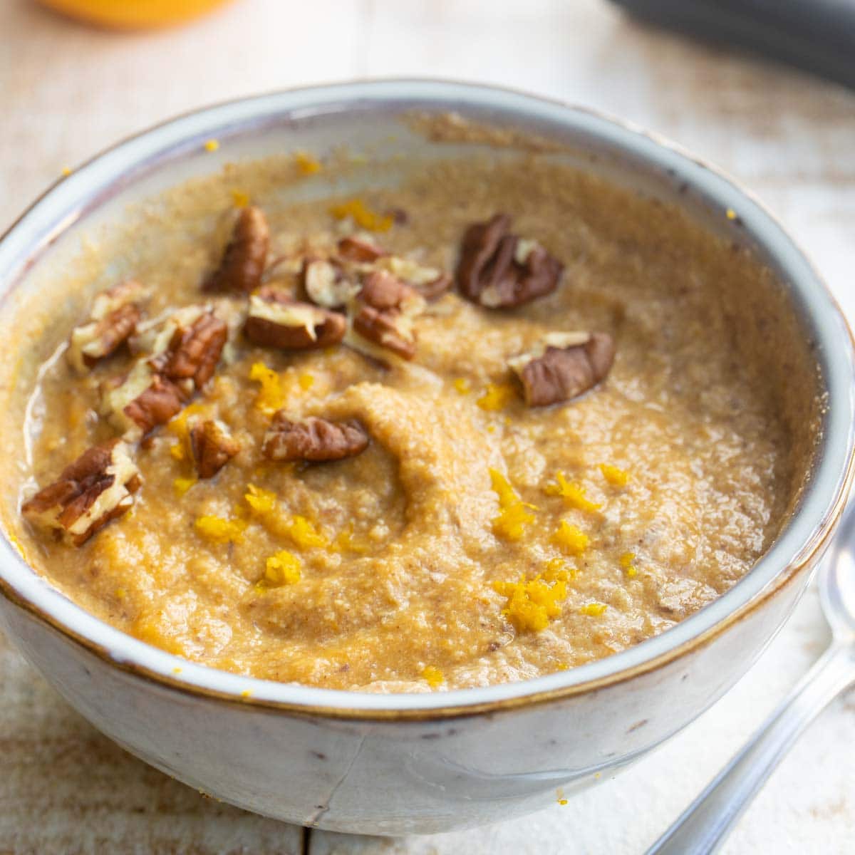 a breakfast bowl with keto pumpkin porridge decorated with crushed pecans and orange zest