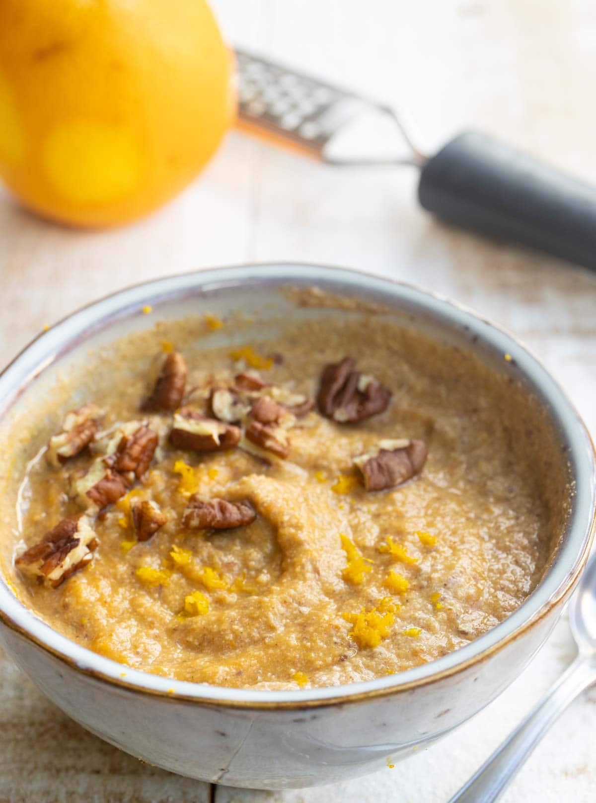 a bowl with pumpkin oatmeal decorated wit pecan nuts and orange zest