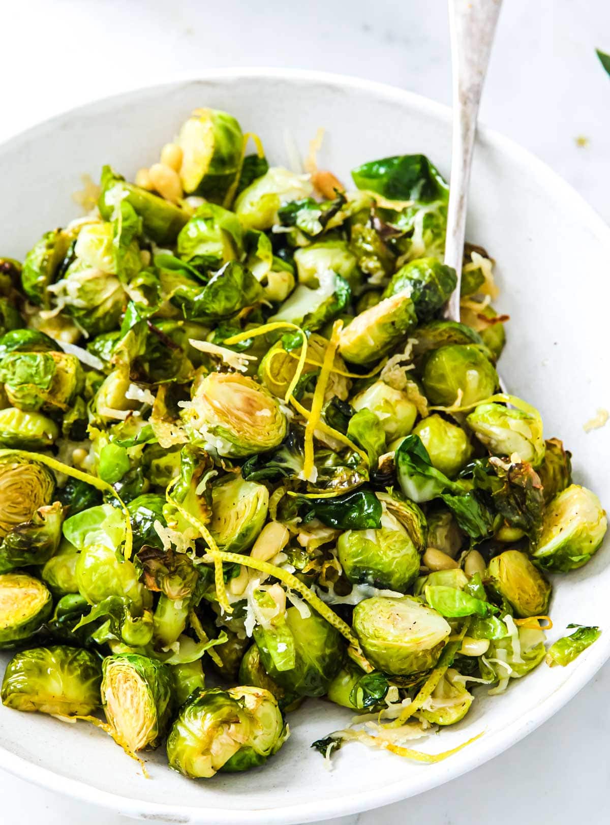 A serving bowl with roasted sprouts, parmesan and lemon zest and a spoon.