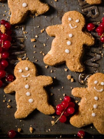 keto gingerbread cookies in the shape of little men with red currants on a baking sheet