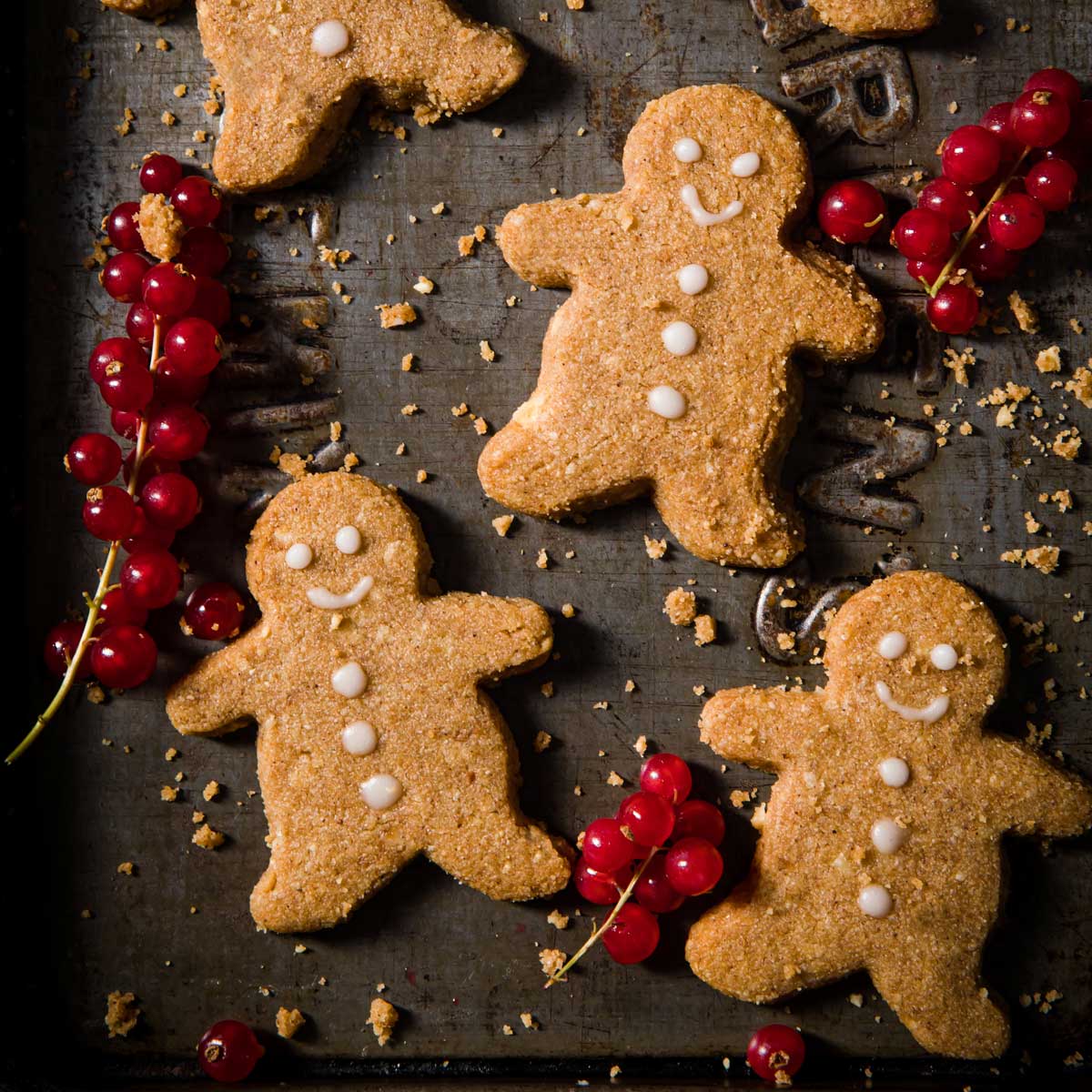 keto gingerbread cookies in the shape of little men with red currants on a baking sheet