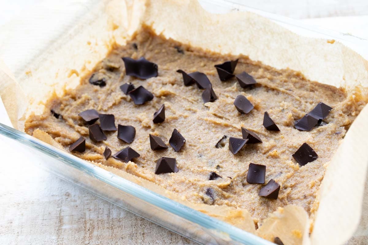 blondie batter in a casserole dish lined with parchment paper