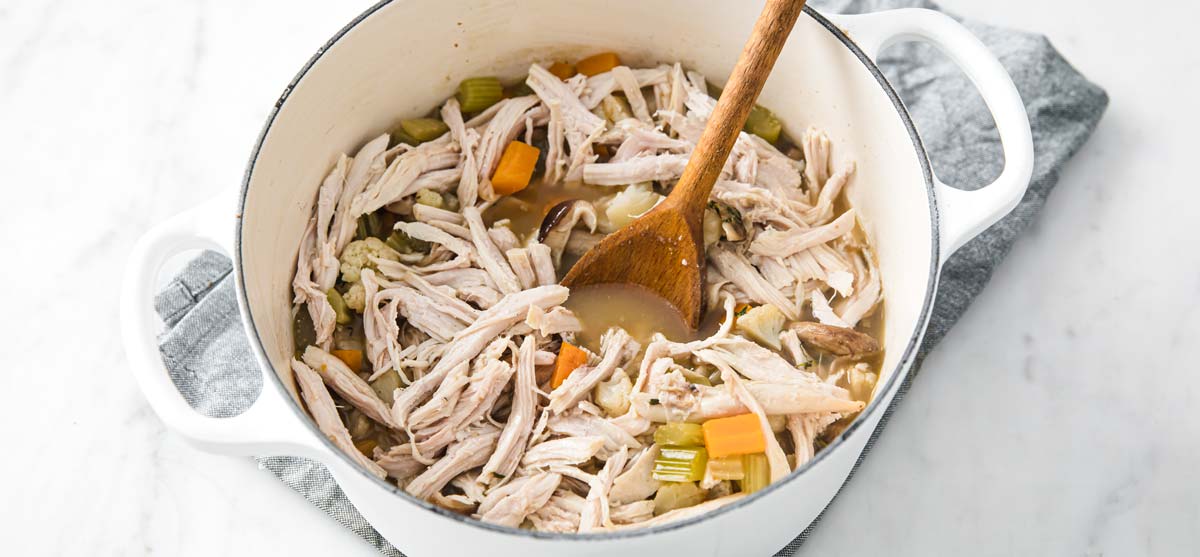 Adding cooked turkey strips to a soup pot.