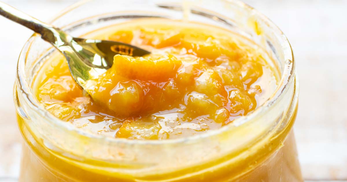 an open jam jar with orange marmalade and a spoon