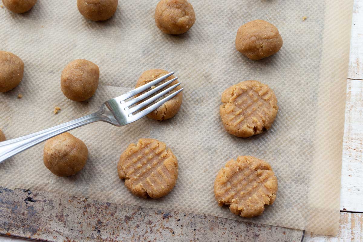 unbaked cookies on a baking sheet and a fork making criss cross patterns
