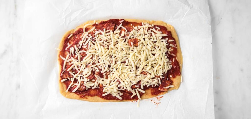 adding tomato paste and cheese on the rolled out dough