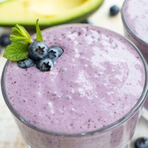 a blueberry smoothie with blueberries and a mint leaf, with half an avocado in the background