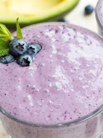 a blueberry smoothie with blueberries and a mint leaf, with half an avocado in the background